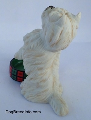 The back left side of a figurine of a West Highland White Terrier figurine in a begging pose with an empty dish. The figurine has fine hair details.