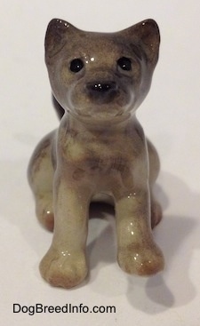 A figurine of a seated gray Wolf cub. The figurine has black circles for eyes.