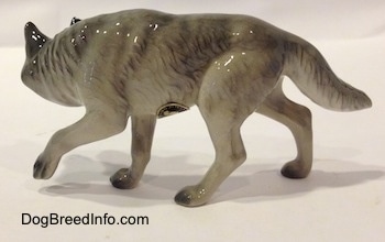 The left side of a stalking figurine of a gray Wolf. The figurine has a long tail.