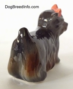 The back right side of a figurine of a gray with brown figurine of a Yorkshire Terrier standing. The figurine is glossy.