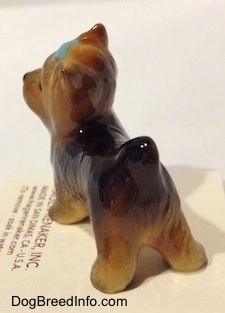 The back left side of a figurine of a black with brown Yorkshire Terrier. The figurine has a short tail that is in the air.