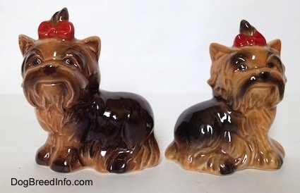 Two black and brown figurines of sitting Yorkshire Terriers. They both have red bows in there hairs.