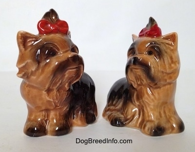 Two black with brown Yorkshire Terrier sitting figurines that are looking each other in the face. They both have black circles for eyes.