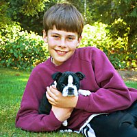 Molly the Boston Terrier in the arms of a boy named Lee who is laying outside and smiling