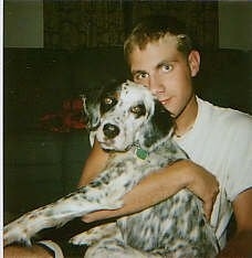 A white and black with brown Llewellin Setter is sitting in a man's lap. The person has their arm wrapped around the body of the dog.