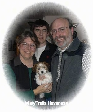 A lady, A man and a boy are standing in a room holding a little puppy in their arms.