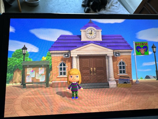 The game character Aries from the island Orion standing in front of resident services with a  yellow bird perched on the bulletin board