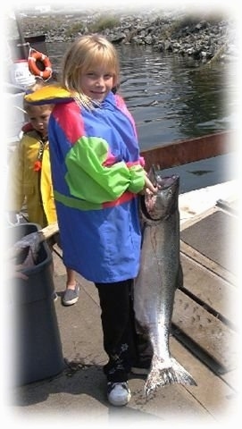 A blonde haired girl is holding a Salmon on a wooden dock.