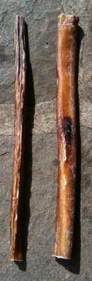 There are two bully stick bones adjacent to each other on a stone porch. One is thin and the other is thick