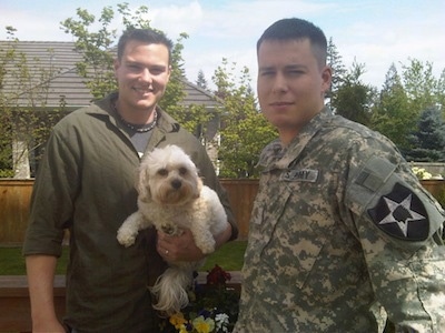 Riley the Cavachon is in the arm of a man who is standing next to another man in a US Army Uniform