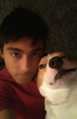 Close Up - A white and tan dog with a black nose and black lips taking a selfie with a boy with dark hair and a red shirt