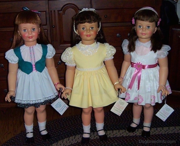 Three real looking large female dolls standing on a blue and white throw rug. 