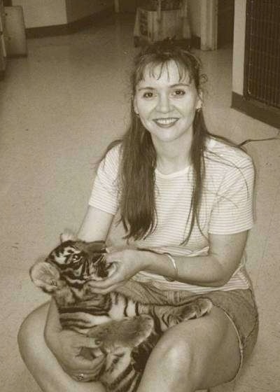 A black and white photo of a lady sitting on a carpeted floor with a Tiger Cub in her lap.
