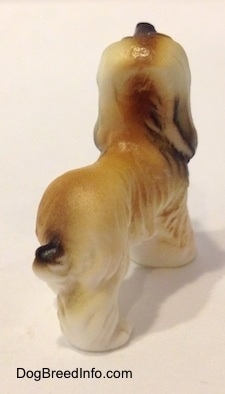The back right side of a white with tan and black tiny vintage bone china Afghan Hound dog figurine. The dog is looking up slightly and holding its tail down low.
