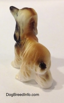 The back left side of a white with tan and black Tiny vintage bone china Afghan Hound dog figurine with long hair drop ears.