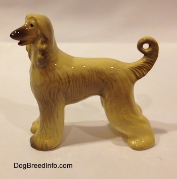 The left side of a tall tan with black Retired Hagen-Renaker Afghan Hound.The dog's long tail curls at the tip making a circle. The legs are thicker because of the breeds thick coat.