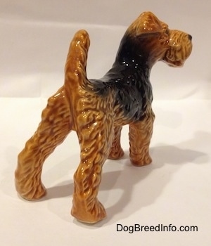 The back right side of a black and brown Vintage Airedale Terrier dog West Germany Goebel figurine with its back legs set wide apart and its tail up in the air.