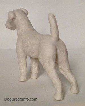 The back left side of a white bisque porcelain Airedale Terrier dog figurine that is unglazed. The dog is leaning forward.