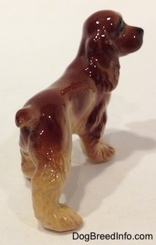 The back right side of a brown and tan ceramis Cocker Spaniel figurine. Its paws have detailed brushings.