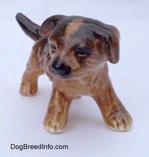 The front right side of a brown and black porcelain Aussie puppy figurine. The figurine has fine paw details.