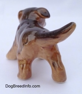 The back of a brown and black porcelain Aussie puppy figurine. The tail of the figurine is swinging to the right.