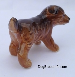 The back right side of a brown and black porcelain Aussie puppy figurine. It has a small amount of hair detail.
