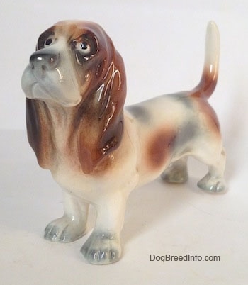The front left side of a white with black and red Basset Hound figurine. The eyes of the figurine are black circles.