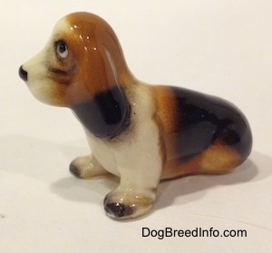 The left side of a black, brown and white ceramic Basset Hound figurine. The ears of the figurine are attached to the neck.