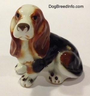 The front left side of a brown, black and white ceramic Basset Hound figurine. The figurine has light face details.