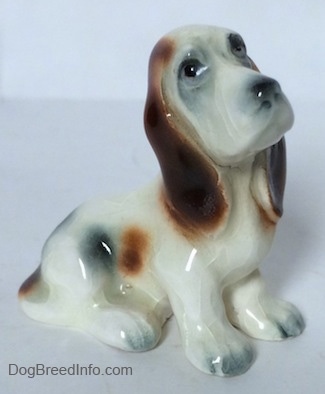 The right side of a white with black and red ceramic Basset Hound figurine. The figurine has black circles for eyes.