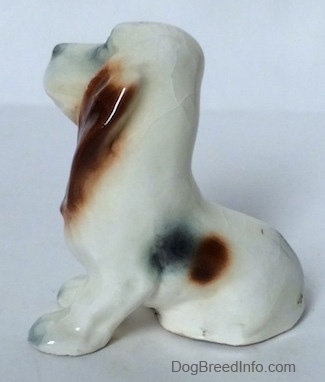 The left side of a white with black and red ceramic Basset Hound figurine. The figurine lacks fine details.