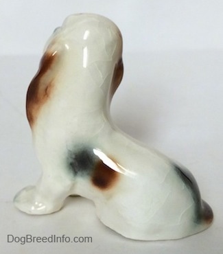 The back left side of a white with black and red ceramic Basset Hound figurine. The figurine is very glossy.