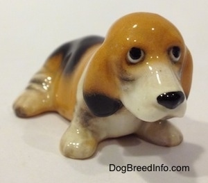 The front right side of a tan and black with white ceramic Basset Hound figurine. The eyes of the figurine are black circles.