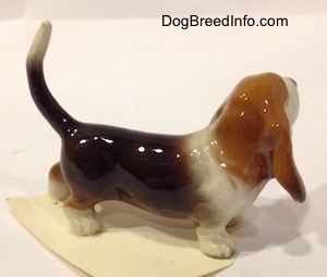 The right side of a black and brown with white Basset Hound figurine. The figurine is very glossy.