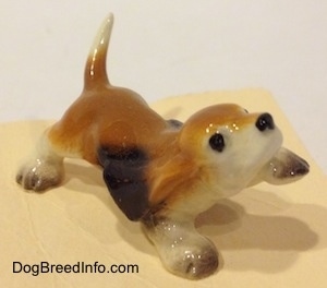 The front left side of a tan with black and white ceramic Basset Hound figurine that has its front left paw in the air. The figurine lacks fine details.
