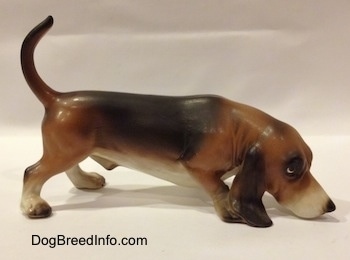 The right side of a brown and black with white porcelain Basset Hound figurine that is sniffing. The ears of the figurine are very detailed.