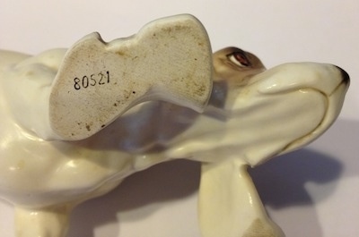 The underside of a white with brown and black porcelain Basset Hound figurine. The figurine has numbers on its feet.