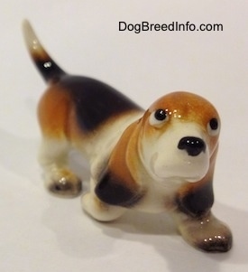 The front right side of a black, tan and white ceramic Basset Hound figurine. The figurine does not have a mouth.