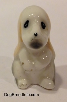 A white with tan and black bone china Basset Hound puppy figurine. The figurine has a black dot for a nose and black circles for eyes.