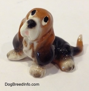 Topdown view of a black and brown with white ceramic Basset Hound figurine that is looking up. The figurine eyes are just black circles.