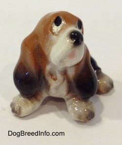 A black and brown with white ceramic Basset Hound figurine that is looking up. The figurines face lacks great detail.
