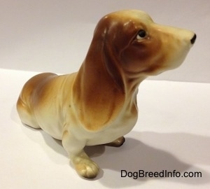 The front left side of a brown and white porcelain Basset Hound figurine. The figurine is painted very great.
