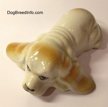 Topdown view of a white with tan porcelain Basset Hound figurine. The back of the figurine is wrinkly.