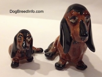 Two, a mother and a puppy, brown and black ceramic Basset Hounds figurines. The figurines lack eye details.