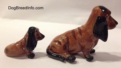 The right side of two, a mother and a puppy, brown and black ceramic Basset Hounds figurines. The figurines are glossy.