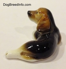 The back of a Cute little black, brown and white porcelain Beagle figurine with two broken front legs. The figurine has detailed ears.