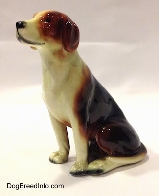 The front left side of a black, brown and white porcelain Beagle figurine. The figurine has black dots for eyes.