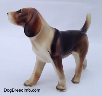 The front left side of a black, brown and white porcelain Beagle Harrier figurine in a standing pose. THe figurine has very detailed ears.