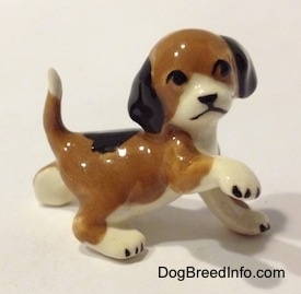 The right side of a brown, black and white miniature Beagle figurine in a standing pose with its paw up. The figurine is very glossy.