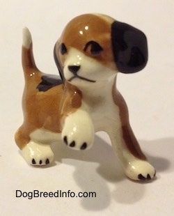 The front right side of a brown, black and white miniature Beagle figurine in a standing pose with its paw up. The figurine has a simple face.